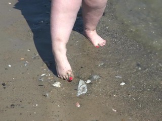 A fat woman with big feet walks along the shore.